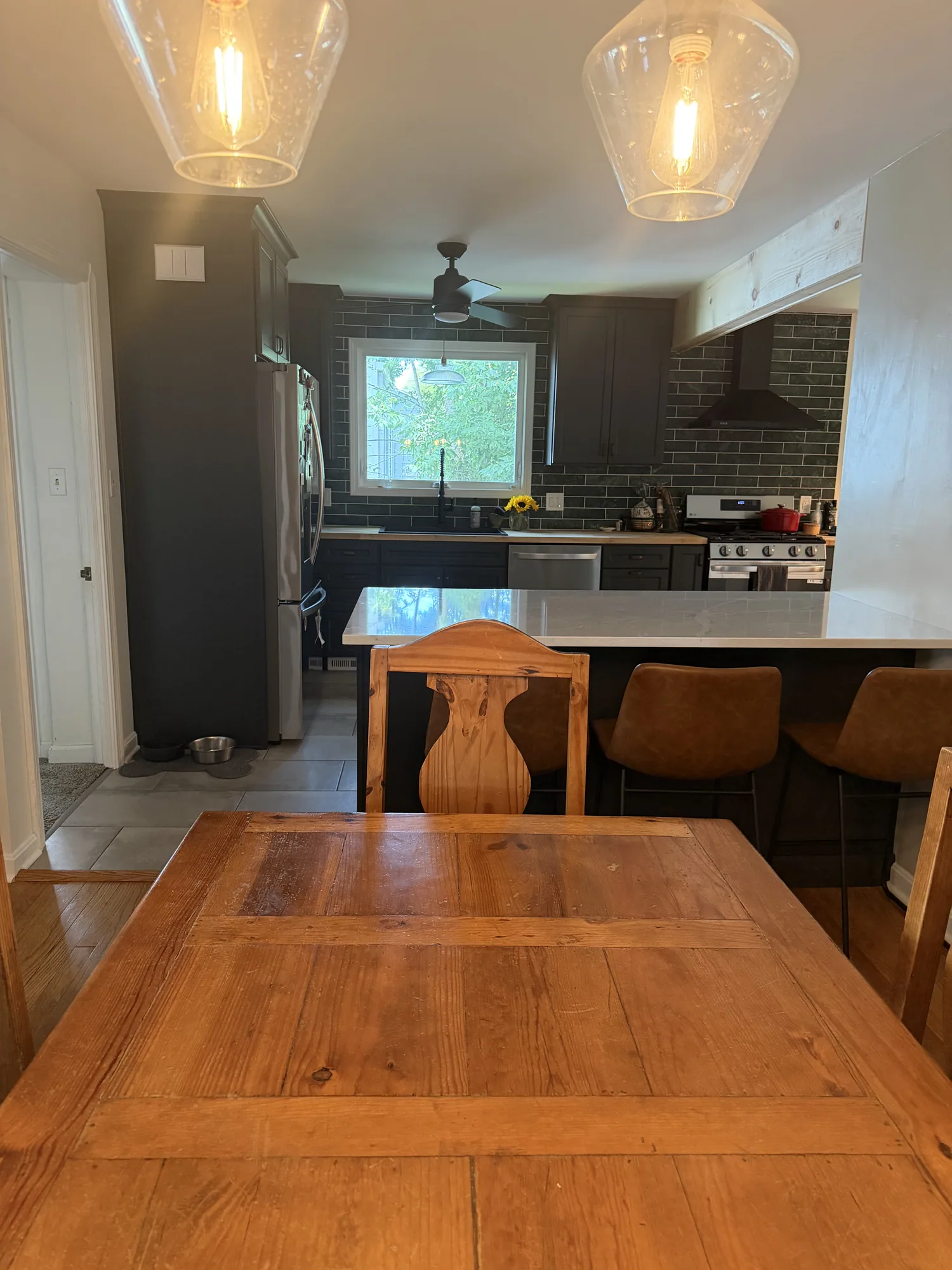 Completed structural kitchen remodel with deep-toned cabinetry, marble backsplash, butcher-block counters, and tile flooring