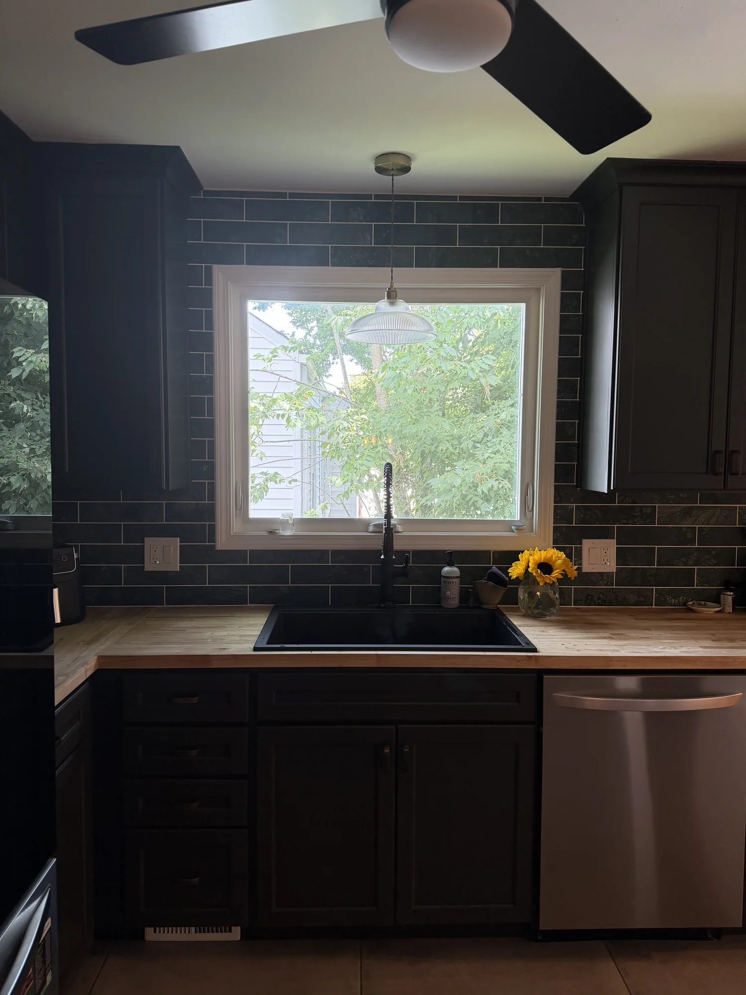 Finished kitchen sink wall with deep-toned cabinetry, real marble tile backsplash, and black sink fixture