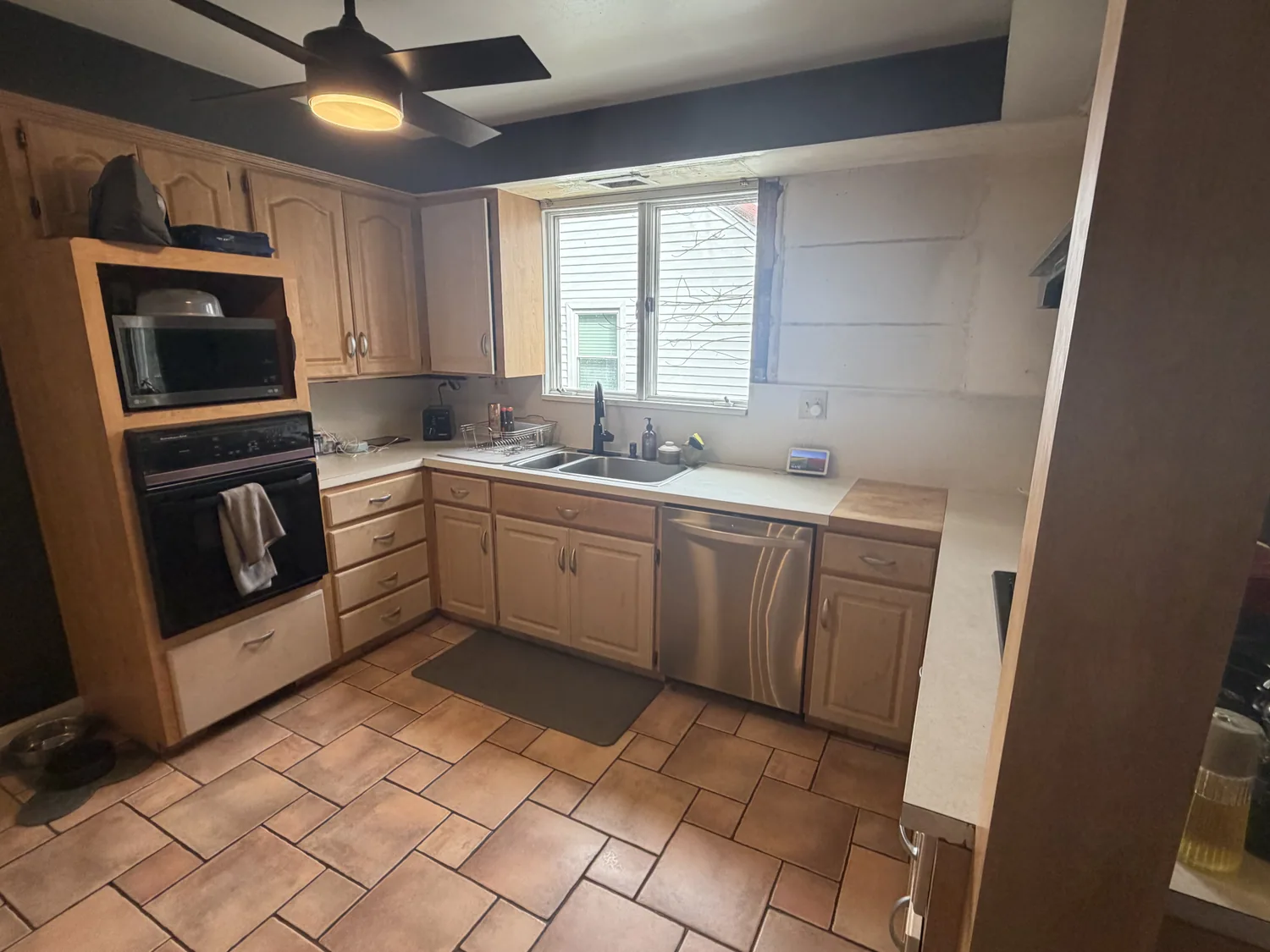 Kitchen before remodeling with light wood cabinets, laminate counters, and small-format floor tile